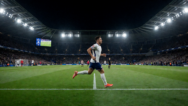 夜间体育场内的比赛直播画面，球员在场上奔跑，看台灯光亮起